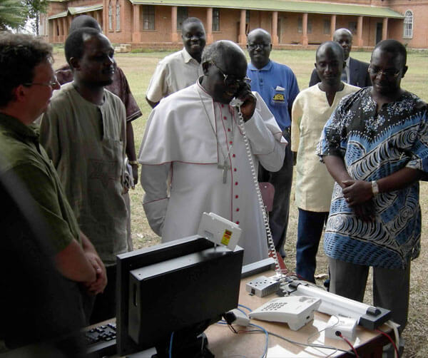 In 2007, Ugandan Archbishop Odama places an internet phone call to an internally-displaced people's camp 70 km away. Internet technologies are encouraging ground-up development like this across the continent. Photo courtesy Bosco-Uganda.