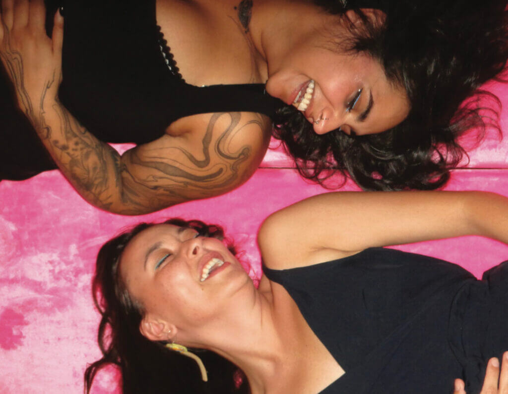 Kiona Callihoo and Sanaa Humayun lounge and laugh together on a fluffy pink blanket